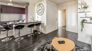 A modern kitchen with dark wood flooring, a central island with bar stools, and a large wall clock. - Apartment Les Alizés  (Bailly-Romainvilliers)