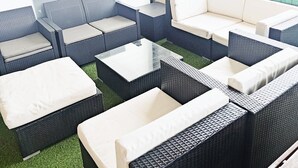 An outdoor seating area with wicker furniture and cushions, a glass coffee table, and a view of a building in the background. - Apartment Les Alizés  (Bailly-Romainvilliers)