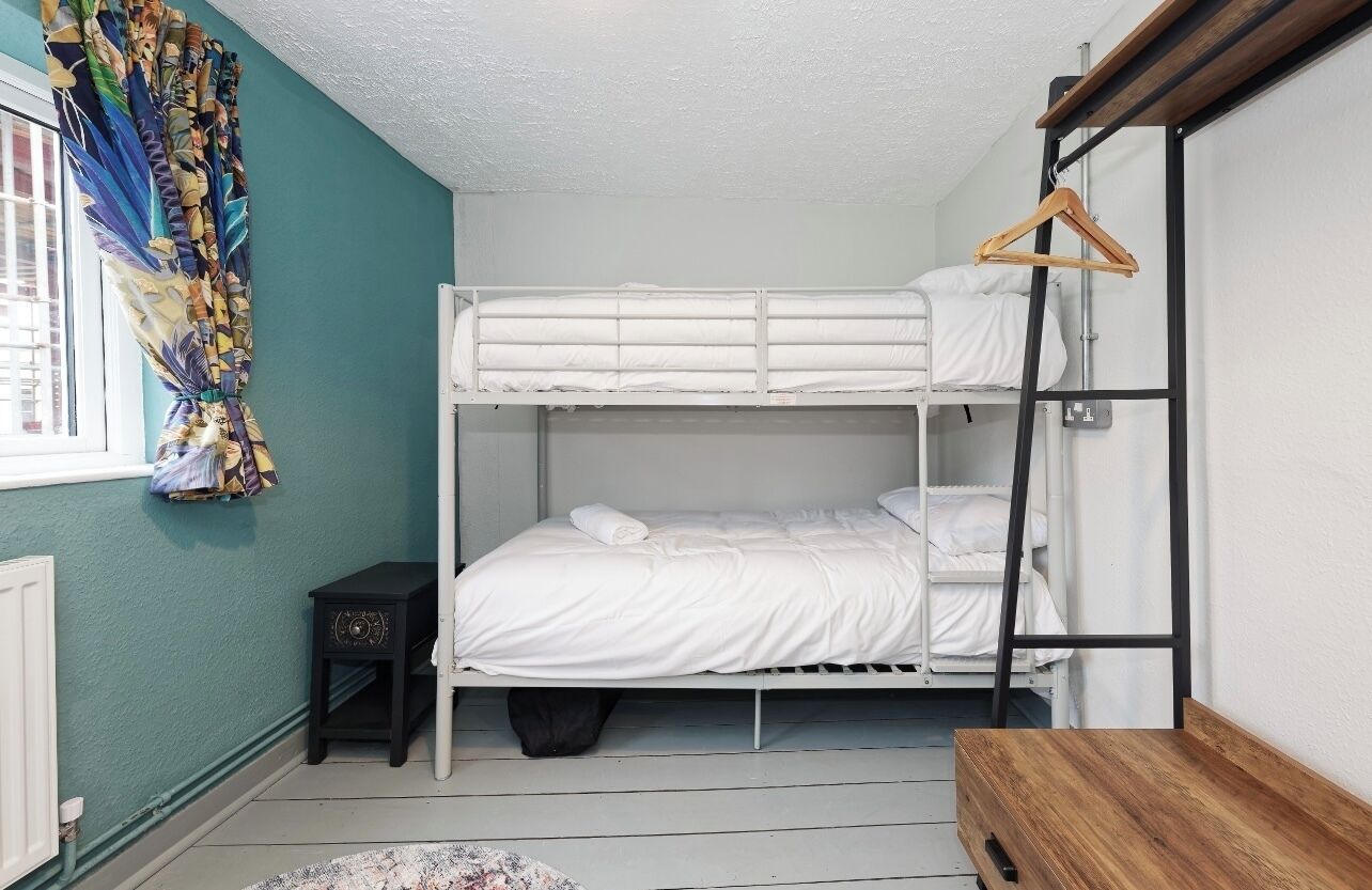 Habitación con literas, un banco de madera, una mesita y una cortina con estampado colorido.