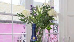 A dining table set for four with a bottle of champagne, a vase of flowers, and empty wine glasses. - The Northern Belle (Margate)