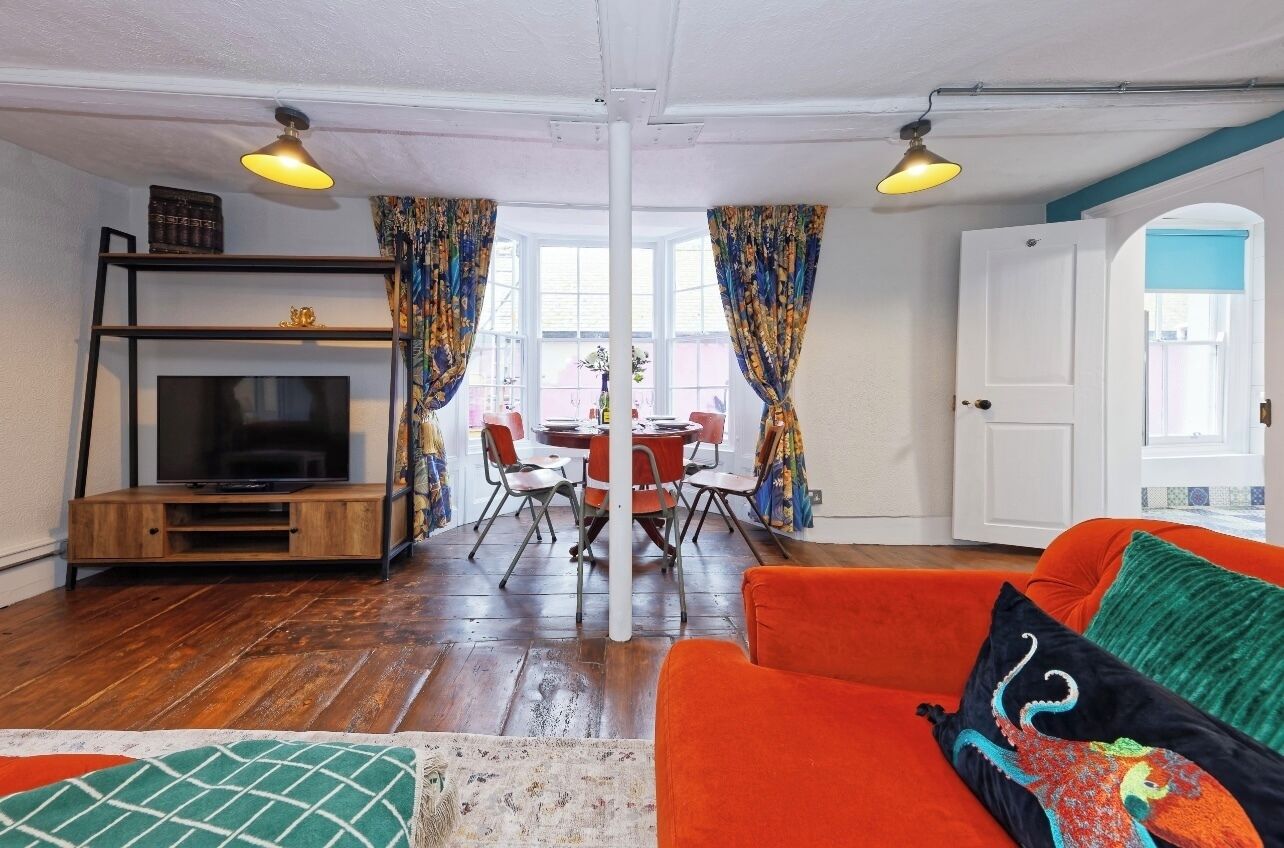 Un salon chaleureux avec un téléviseur, un meuble de rangement en bois, un canapé orange et un coin repas comprenant une table et des chaises.