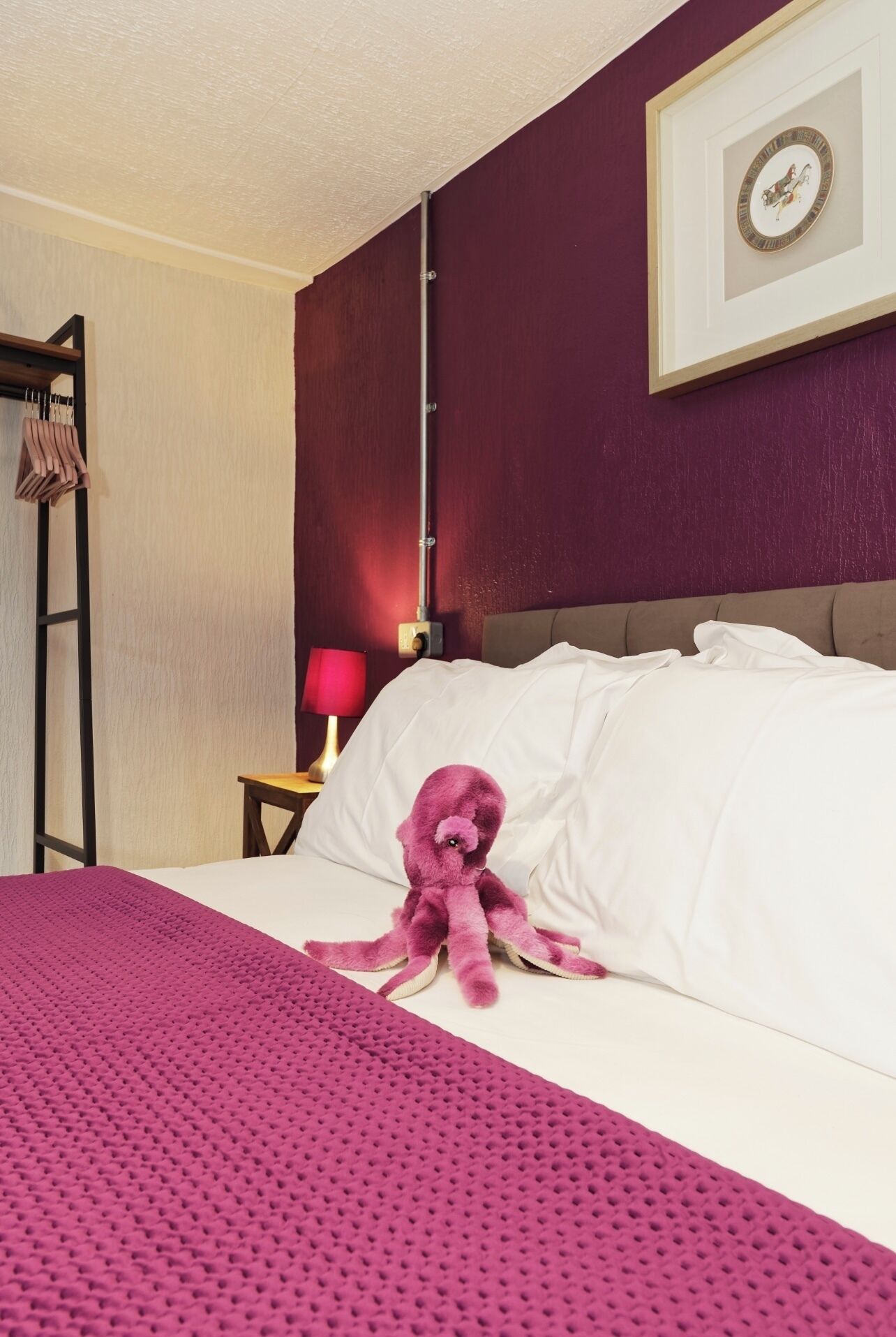 Une chambre d’hôtel avec un lit, une lampe rouge, un tableau encadré au mur et une échelle en bois appuyée contre le mur.