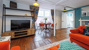 A living room with a flat-screen TV, wooden entertainment unit, orange sofa, and a dining area with a round table and chairs. - The Northern Belle (Margate)