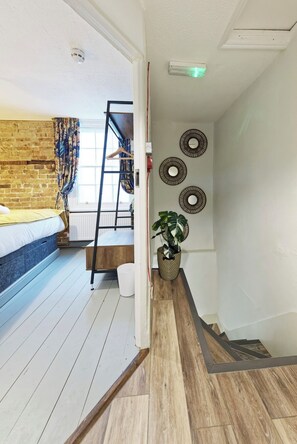 A room with a bunk bed, a wooden floor, a staircase, and a potted plant. - The Northern Belle (Margate)