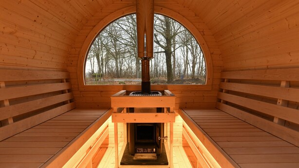 A wooden sauna with a large arched window, a central heating element, and benches around the perimeter. - Beautiful home in Brørup with WiFi (Brørup)