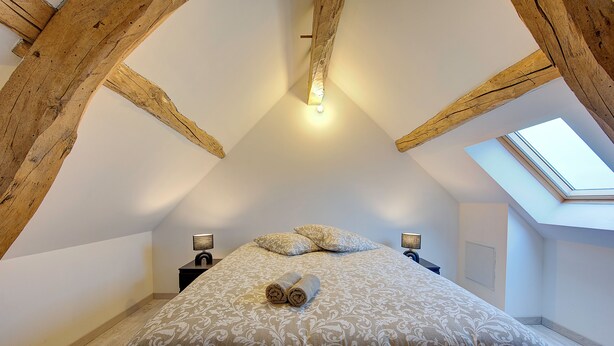 Une chambre à coucher avec un plafond en voûte, un puits de lumière, un lit avec des serviettes roulées et des lampes de chevet.