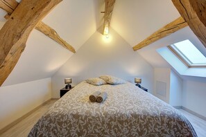 Un dormitorio con techo abovedado, tragaluz, cama con toallas enrolladas y lámparas de noche.