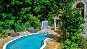 Una piscina con sillas de descanso, rodeada de exuberante vegetación y un pabellón.