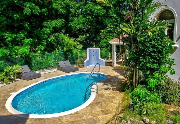 A swimming pool with lounge chairs, surrounded by lush greenery and a gazebo.