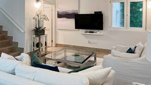 Una sala de estar moderna con una mesa de centro de vidrio, sofás blancos, un televisor de pantalla plana y obras de arte en la pared.