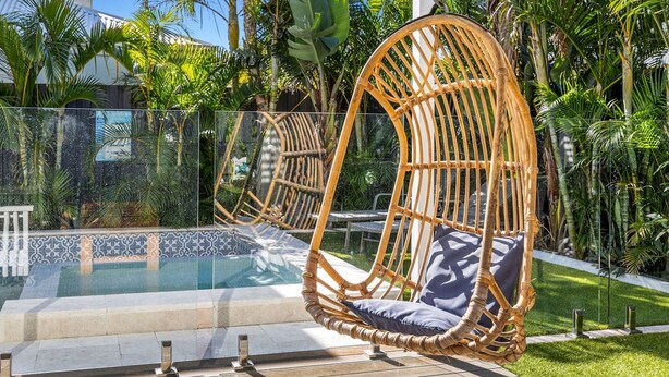 Ein Korbstuhl mit Kissen an einem Pool mit Glasboden, umgeben von tropischen Pflanzen.