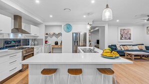 Eine moderne Küche mit einer zentralen Kochinsel, Barhocker, einem Kühlschrank und einem Essbereich mit einer Couch und einem Couchtisch.