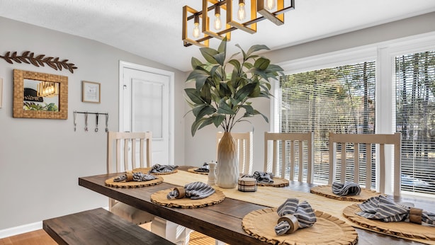 A dining area with a wooden table set for four, surrounded by chairs, a large plant, and a modern light fixture. - Cozy & fun getaway on the water near Myrtle Beach! (Conway)