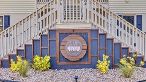 A building entrance with a wooden staircase, a sign reading "Wild River Risin," and a gravel pathway with yellow plants. - Cozy & fun getaway on the water near Myrtle Beach! (Conway)