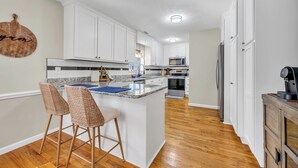 A modern kitchen with white cabinets, a granite countertop, and a central island with bar stools. - Cozy & fun getaway on the water near Myrtle Beach! (Conway)