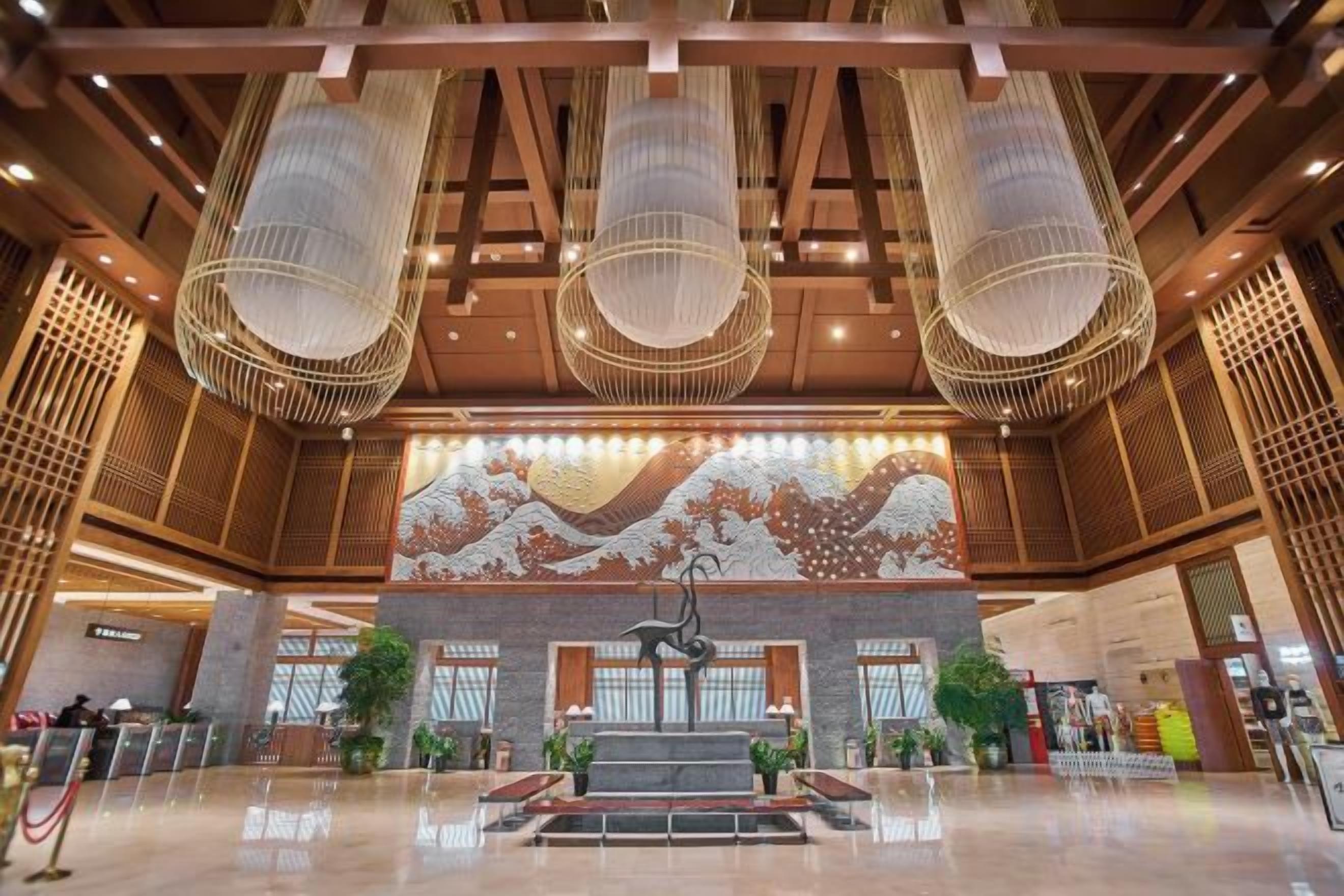 A spacious lobby with a central staircase, large hanging light fixtures, and a decorative wall mural.