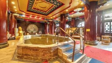 A hot tub with a stone base, surrounded by wooden columns and a colorful ceiling.