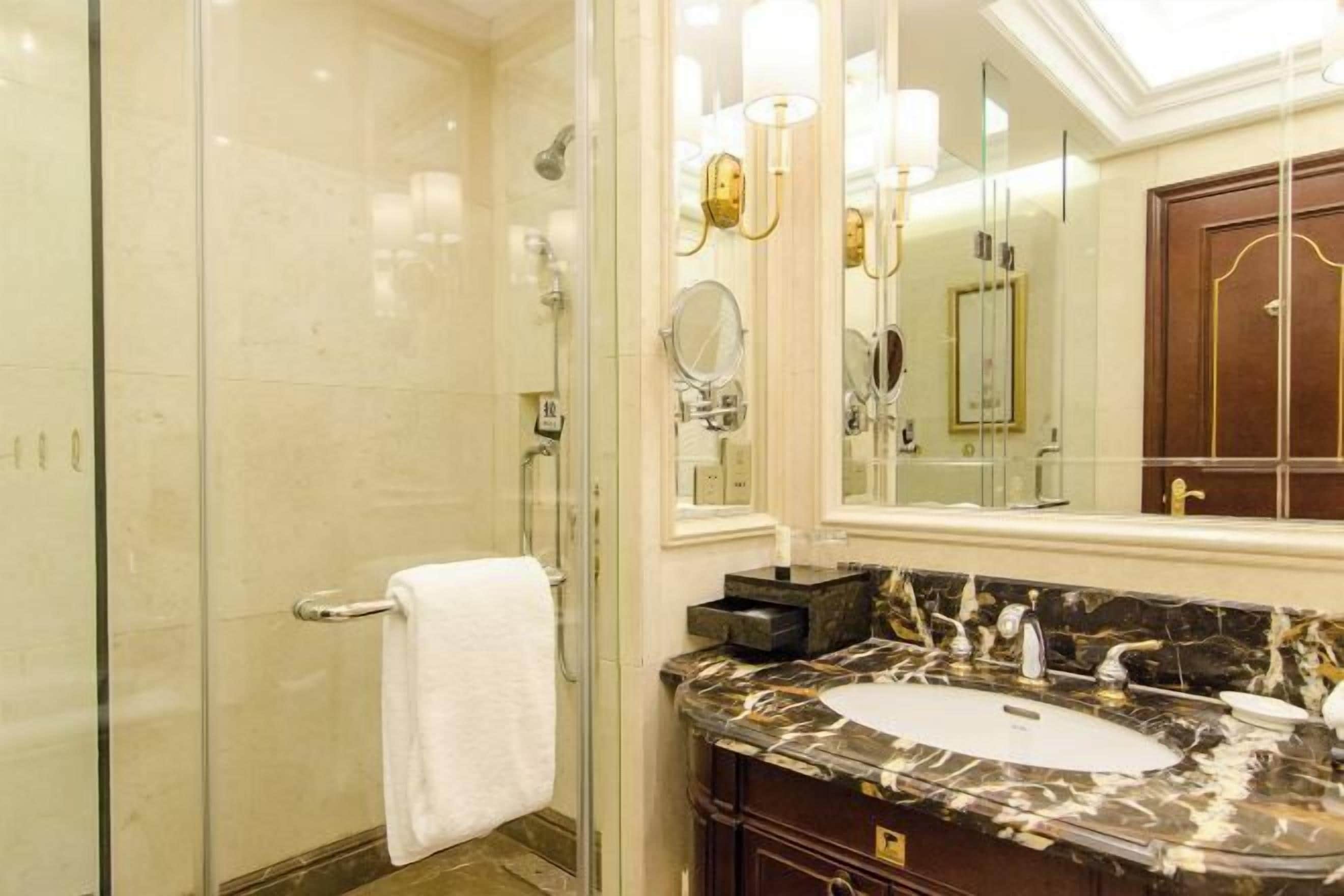 A bathroom with a glass shower enclosure, a white sink with a marble countertop, and a large mirror above the sink.