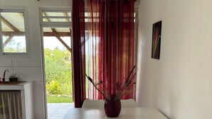A dining area with a white table, two white chairs, a potted plant, and a view of greenery outside. - Kaz Ti Plézi (Capesterre-de-Marie-Galante)