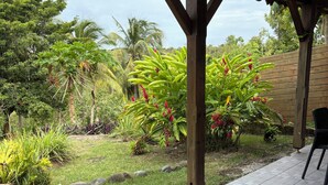 A covered patio area with a tiled floor, surrounded by lush greenery and a wooden fence. - Kaz Ti Plézi (Capesterre-de-Marie-Galante)