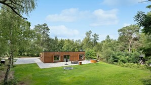 A modern wooden cabin with a patio, surrounded by lush greenery and trees.