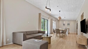 A modern living room with a sectional sofa, ottoman, round coffee table, dining area with chairs, and a kitchen island.