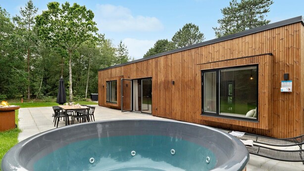 A modern wooden building with a hot tub, outdoor seating, and a patio area.