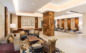 Un hall d’entrée spacieux avec une colonne centrale en bois, un coin salon avec des canapés et des fauteuils, et des œuvres d’art encadrées accrochées aux murs.
