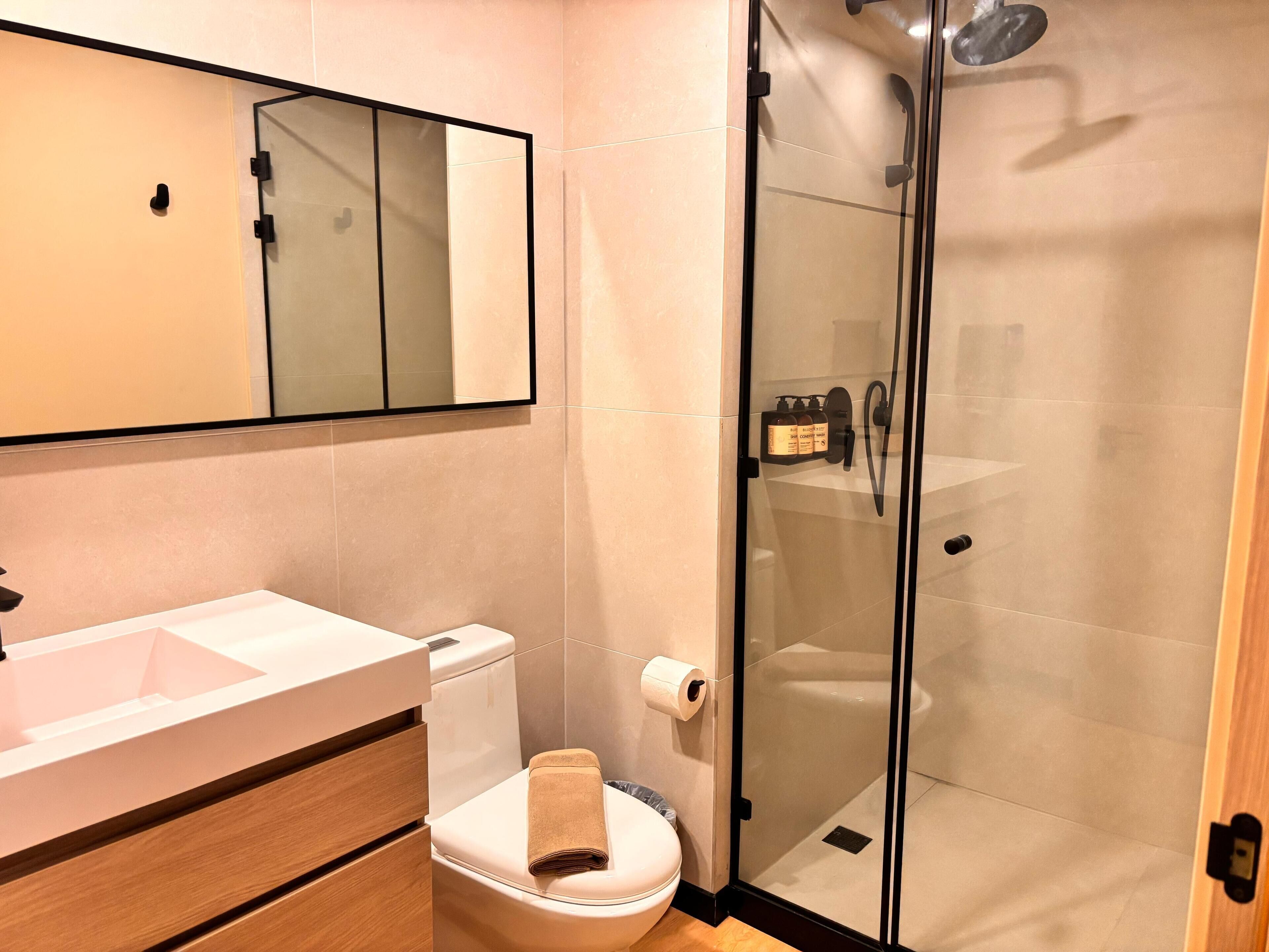 Ein modernes Badezimmer mit Duschkabine aus Glas, Waschbecken in Weiß und Toilette mit Handtuch darauf.