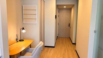 A hallway with a wooden floor, a desk with a chair, a lamp, and a framed picture on the wall.
