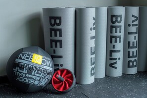 Una hilera de objetos cilíndricos con el texto “BEE-LIV”, un objeto negro y rojo con texto y gráficos, y una superficie texturizada.