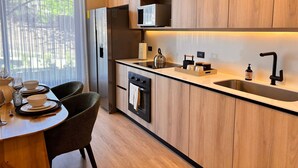 A modern kitchen with wooden cabinets, a stainless steel sink, and a dining area with a table set for two. - BEE Suites San José - Santa Ana (Santa Ana)