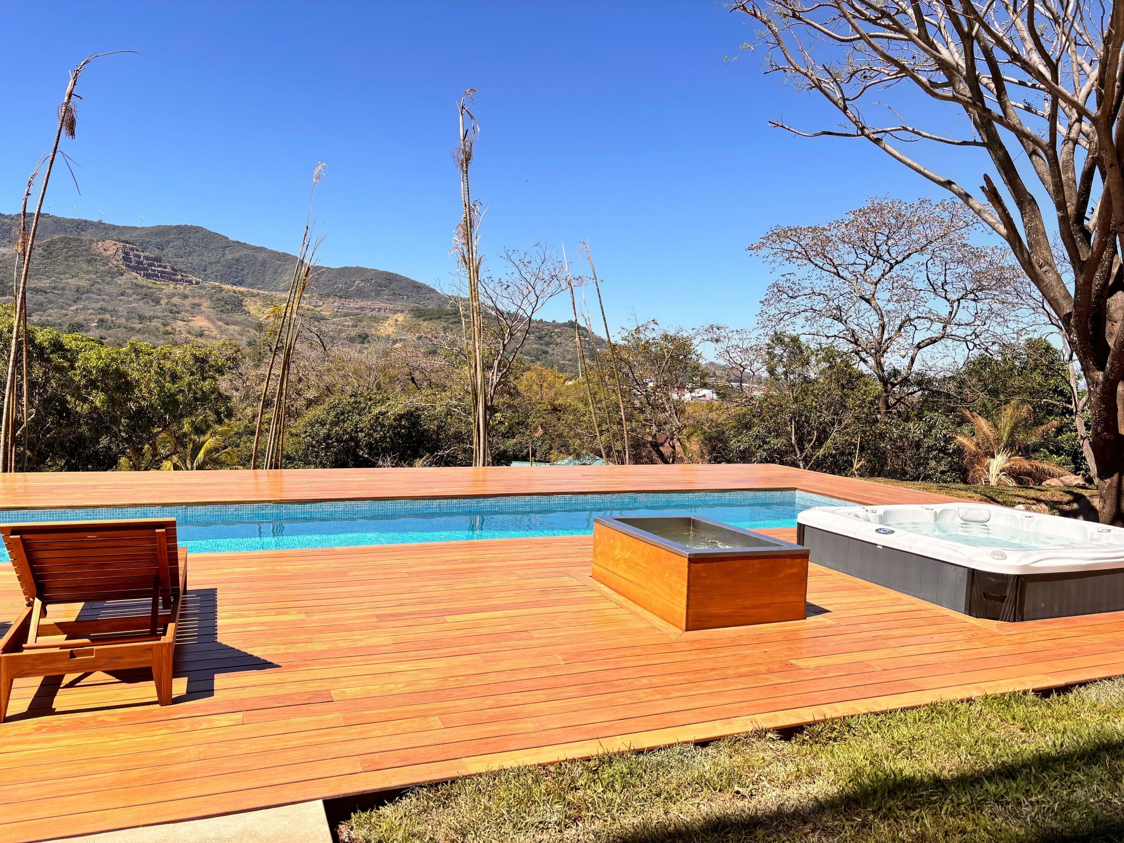 Una terraza de madera con piscina, jacuzzi y una silla de descanso.