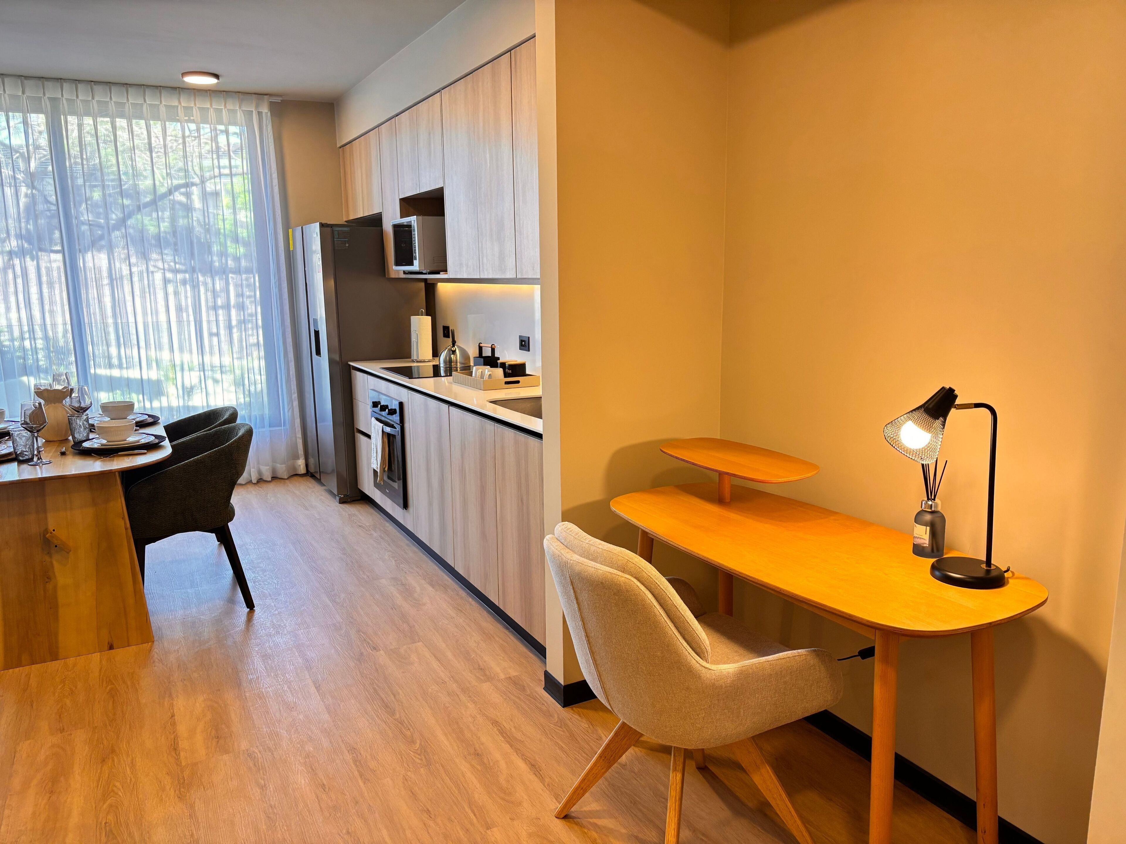A modern kitchen with a dining area, a small table with a lamp, and a chair.