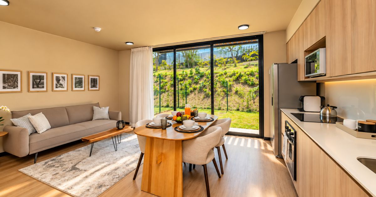 A modern kitchen with a dining area, large windows, and a view of a garden.