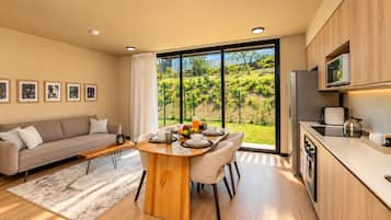A modern kitchen with a dining area, large windows, and a view of a garden.