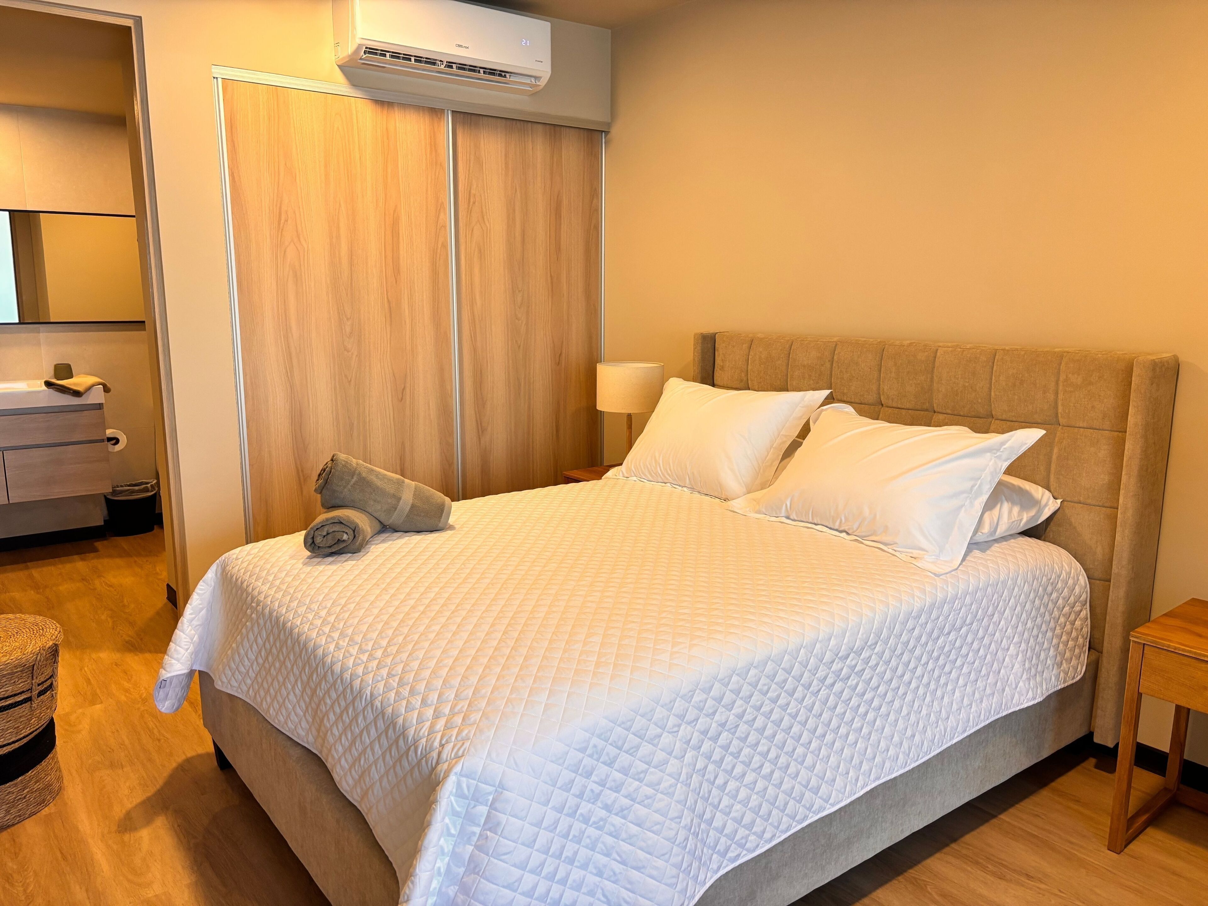 A neatly made bed with white bedding, a wooden headboard, and a bedside lamp.