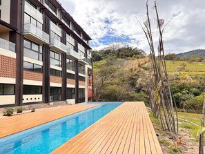 A modern building with a pool area, wooden deck, and a view of the surrounding landscape.