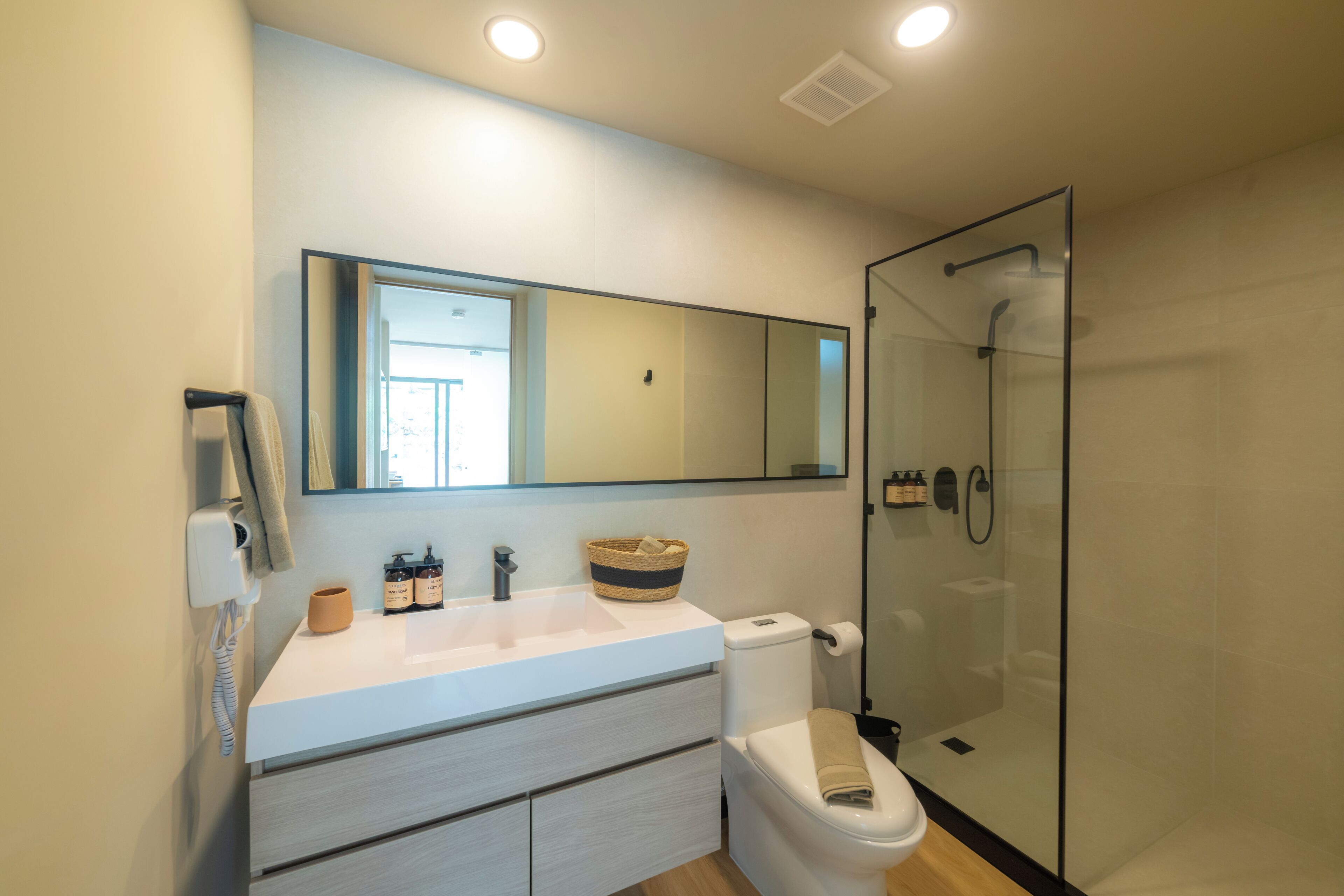 A modern bathroom with a glass shower enclosure, a white sink with a mirror above, and a toilet with a beige towel on it.