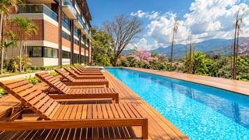 A swimming pool with wooden loungers and a view of a modern building with a brick facade.