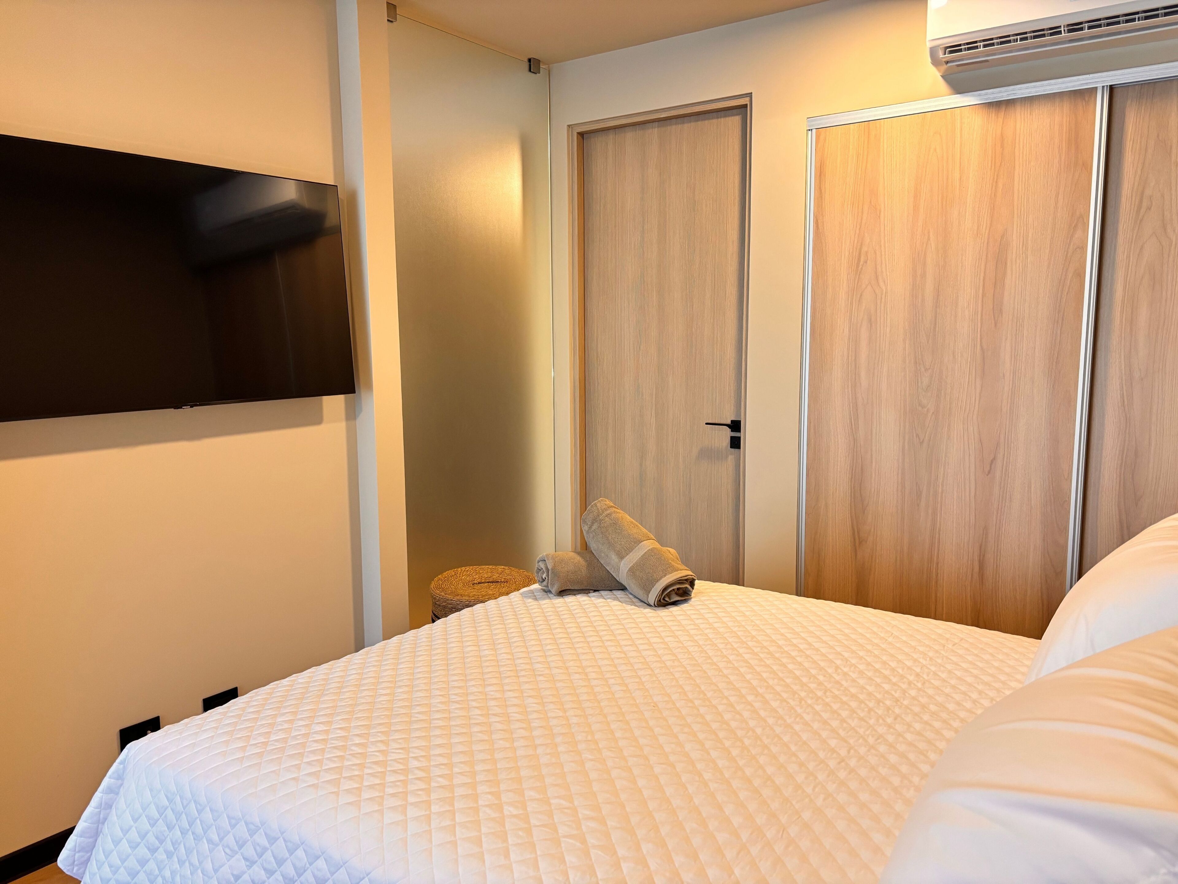 Una habitación de hotel con una cama, un televisor de pantalla plana montado en la pared y un armario de madera.