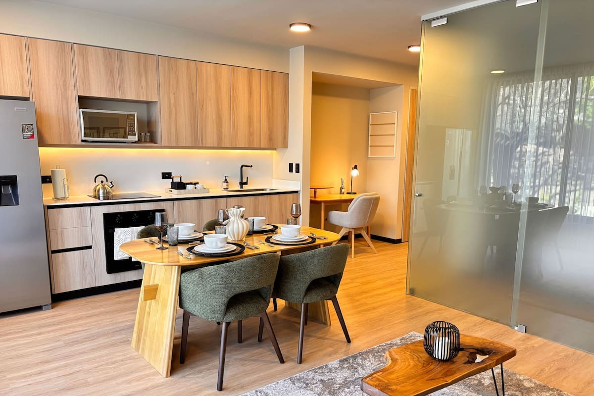 A modern kitchen with wooden cabinets, a microwave, and a dining area with two chairs and a table set for two.