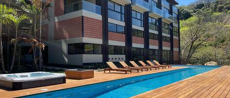 A modern hotel with a swimming pool, lounge chairs, and a hot tub.