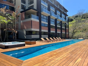Un hotel moderno con piscina, sillas de descanso y bañera de hidromasaje.