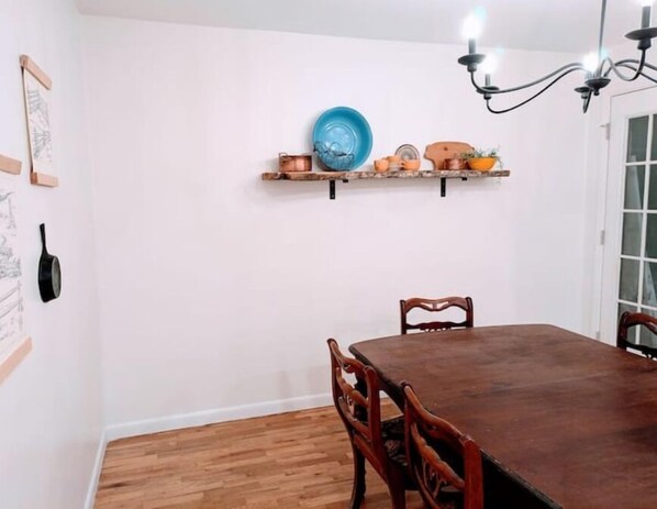 Zona pranzo con tavolo e sedie in legno, un lampadario e mensole a parete con stoviglie e un piatto blu.