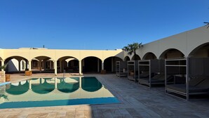 Un área de piscina con una piscina azul cristalina, suelo de piedra y una serie de arcos.