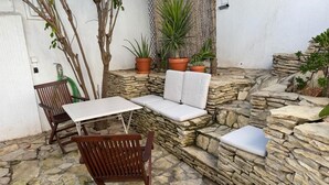 Un área de estar al aire libre con muros de piedra, sillas de madera y un banco acolchado.