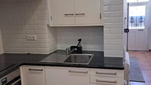Una cocina con armarios blancos, encimera negra y pileta de acero inoxidable.