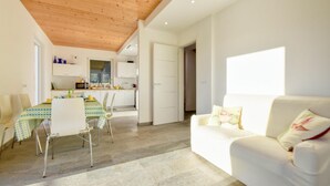 Un salon moderne avec un plafond en bois, un coin repas avec une table et des chaises, et une cuisine en arrière-plan.