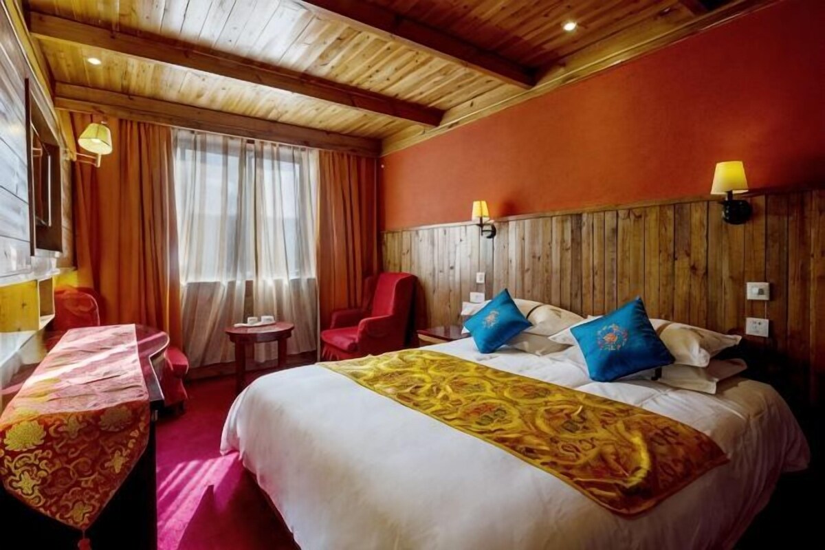 Une chambre d’hôtel avec un lit, un bureau, une chaise, une petite table et une fenêtre avec des rideaux.